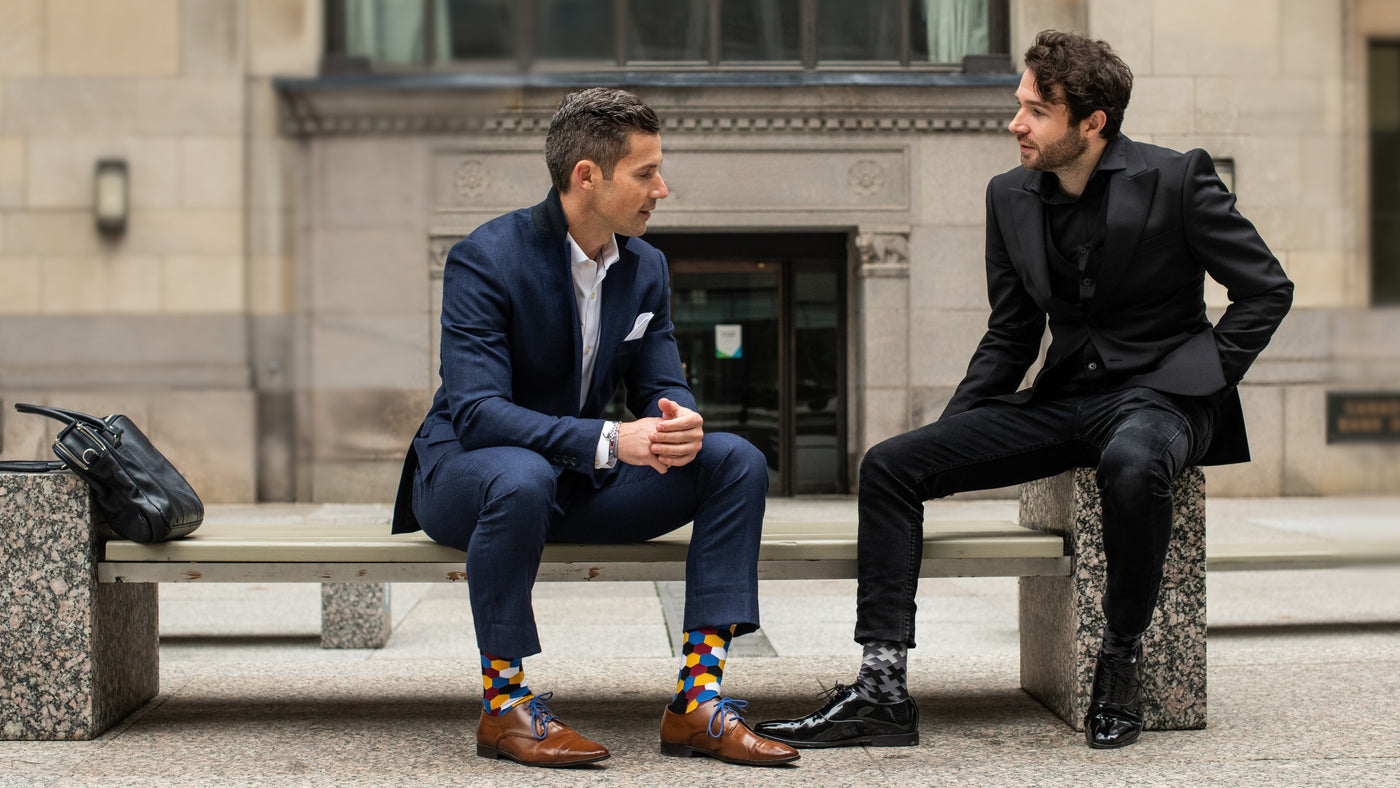 two men sitting on a bench wearing suits and men's dress socks